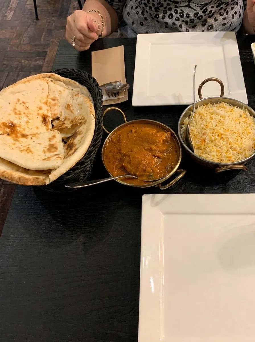 Twee karahi's met curry naast een mand met naan
